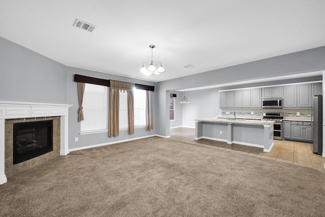 unfurnished living room featuring visible vents, light carpet, a tiled fireplace, a sink, and a notable chandelier