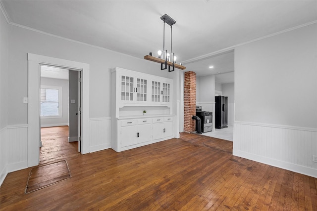unfurnished dining area with a notable chandelier, dark wood finished floors, ornamental molding, and a wainscoted wall