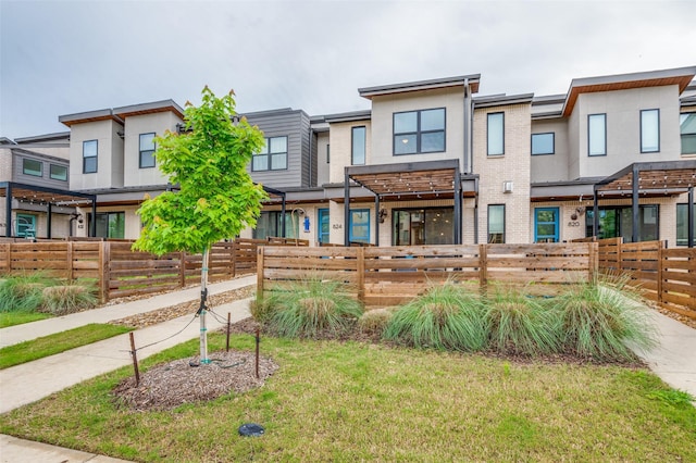 townhome / multi-family property featuring a front yard, fence private yard, and brick siding