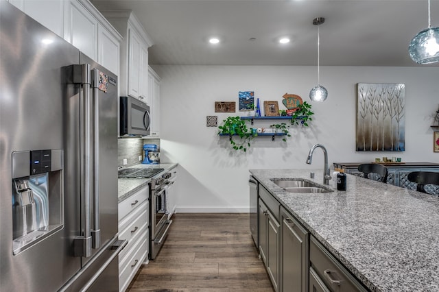 kitchen featuring dark wood-style flooring, light stone countertops, appliances with stainless steel finishes, a sink, and white cabinetry