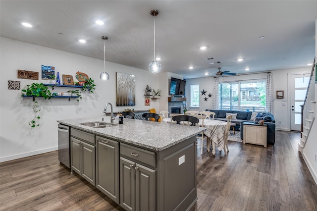 kitchen featuring a sink, dishwasher, a fireplace, gray cabinetry, and a center island with sink