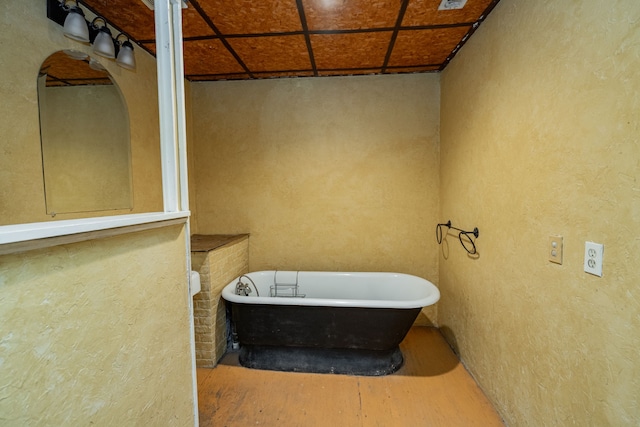 bathroom with a textured wall, a freestanding tub, and wood finished floors