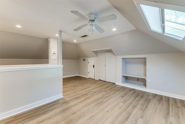 additional living space featuring ceiling fan, vaulted ceiling with skylight, built in shelves, baseboards, and visible vents