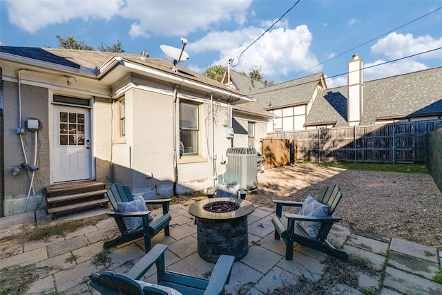 back of property with brick siding, a fenced backyard, an outdoor fire pit, and central AC