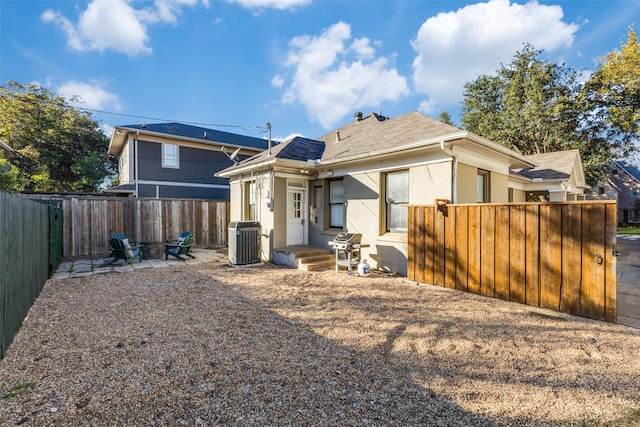 back of house featuring brick siding, central AC unit, a fenced backyard, and roof with shingles