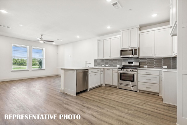 kitchen with light wood-style flooring, stainless steel appliances, a peninsula, decorative backsplash, and visible vents