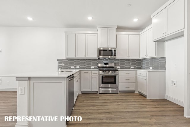 kitchen with decorative backsplash, appliances with stainless steel finishes, a sink, a peninsula, and light wood-style floors
