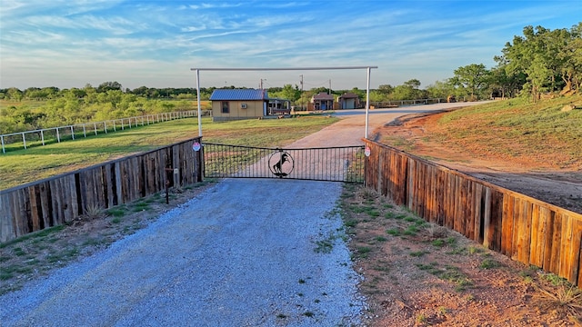 view of street featuring a gate, a gated entry, driveway, and a rural view