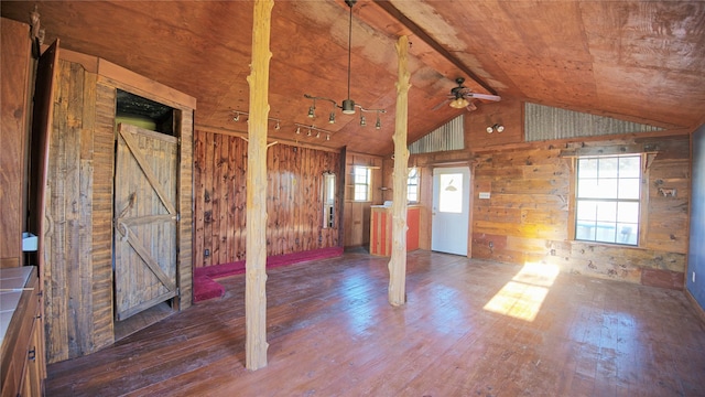 interior space with ceiling fan, vaulted ceiling, wood walls, hardwood / wood-style flooring, and a barn door