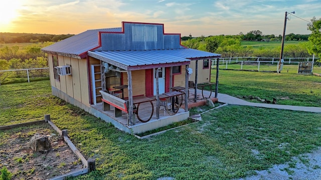 outdoor structure at dusk featuring fence, a lawn, and an AC wall unit