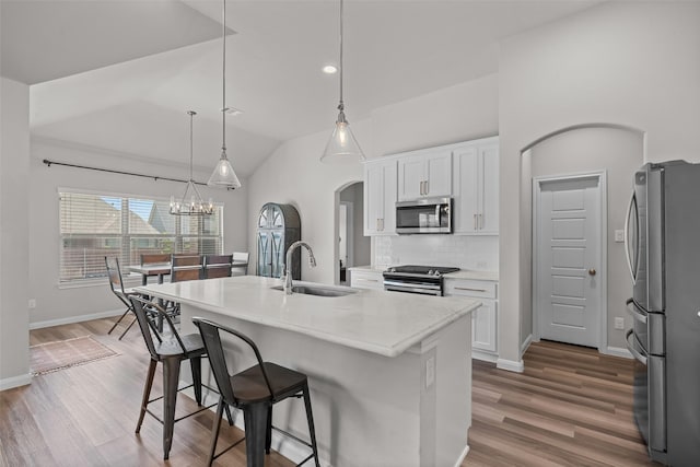 kitchen featuring arched walkways, a sink, white cabinets, a breakfast bar, and stainless steel appliances