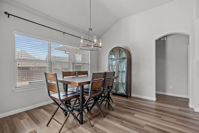 dining space featuring baseboards, a chandelier, arched walkways, light wood finished floors, and vaulted ceiling