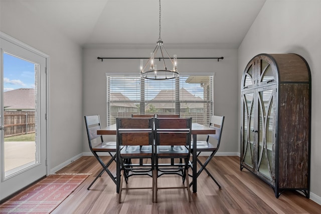 dining space with an inviting chandelier, a healthy amount of sunlight, wood finished floors, and vaulted ceiling