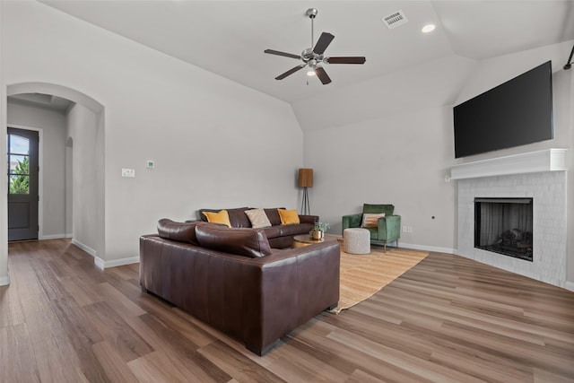 living area with ceiling fan, arched walkways, a brick fireplace, wood finished floors, and baseboards