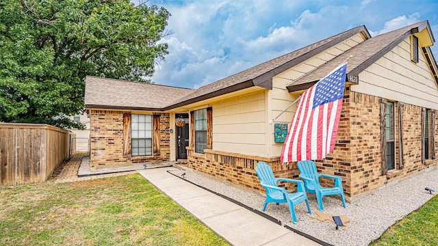 view of front of house with fence, roof with shingles, brick siding, a front yard, and a patio