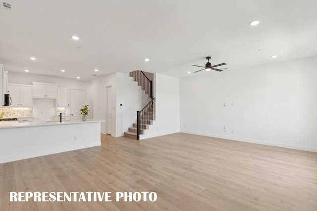 unfurnished living room featuring ceiling fan, stairway, baseboards, light wood finished floors, and recessed lighting