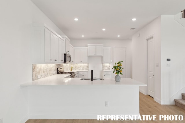 kitchen with decorative backsplash, a peninsula, light countertops, a sink, and stainless steel appliances