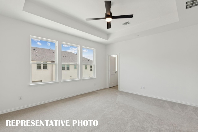 unfurnished room featuring carpet flooring, a ceiling fan, visible vents, and a raised ceiling