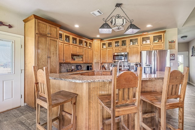 kitchen featuring decorative backsplash, visible vents, appliances with stainless steel finishes, brown cabinets, and dark wood finished floors