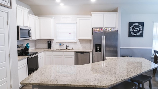 kitchen with decorative backsplash, a kitchen bar, appliances with stainless steel finishes, a sink, and white cabinetry