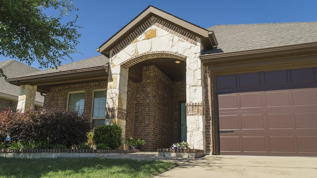 entrance to property with brick siding, a shingled roof, and a garage