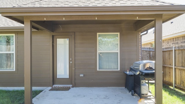 property entrance with a patio, fence, and a shingled roof
