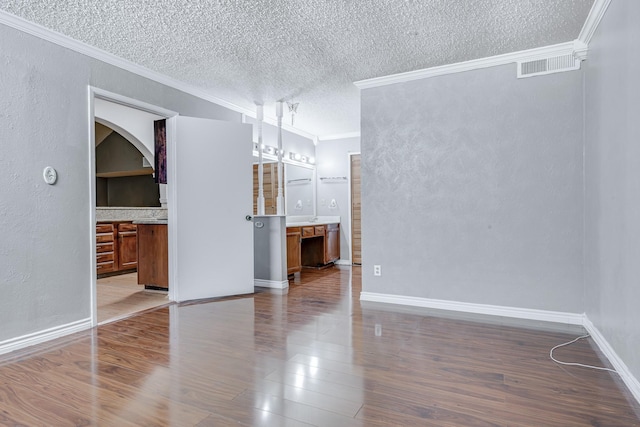 unfurnished dining area featuring a textured ceiling, visible vents, crown molding, dark wood finished floors, and baseboards