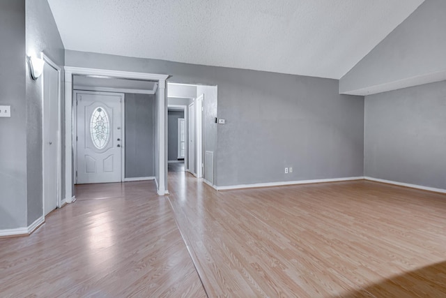 foyer featuring baseboards, a textured ceiling, light wood-style flooring, and lofted ceiling