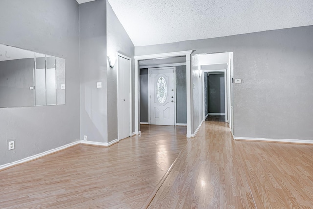 foyer featuring light wood-type flooring, a textured ceiling, baseboards, and lofted ceiling