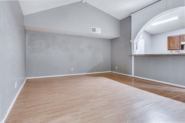 unfurnished living room featuring arched walkways, baseboards, wood finished floors, lofted ceiling, and visible vents