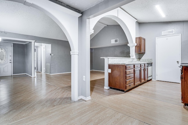 interior space with a textured ceiling, visible vents, arched walkways, light wood-type flooring, and baseboards