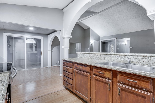 kitchen featuring light wood-style floors, ornate columns, arched walkways, a sink, and vaulted ceiling