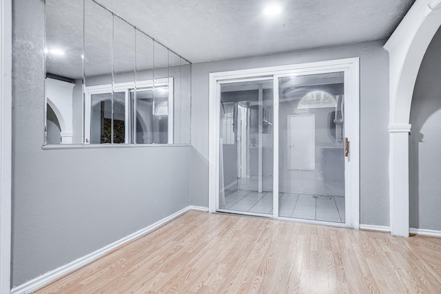 unfurnished bedroom with arched walkways, baseboards, and wood finished floors