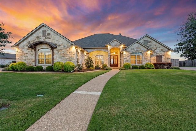 french country style house with a yard, roof with shingles, and stone siding