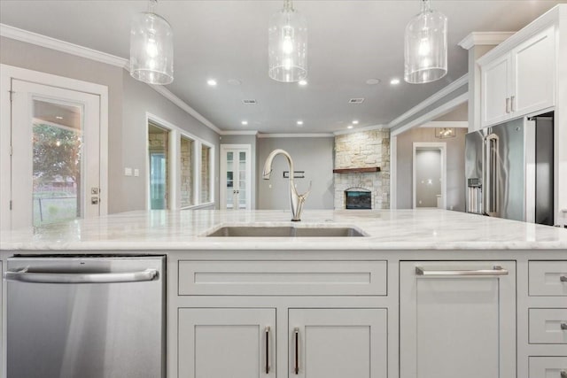 kitchen with light stone countertops, a sink, ornamental molding, stainless steel appliances, and white cabinetry