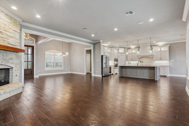 unfurnished living room with dark wood-style flooring, a fireplace, baseboards, an inviting chandelier, and ornamental molding