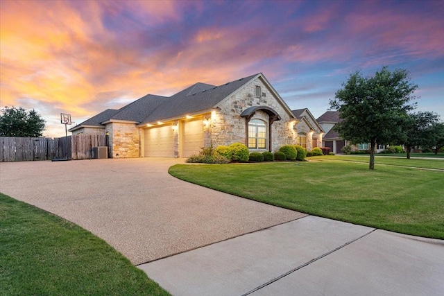 french country style house featuring a garage, fence, stone siding, concrete driveway, and a yard