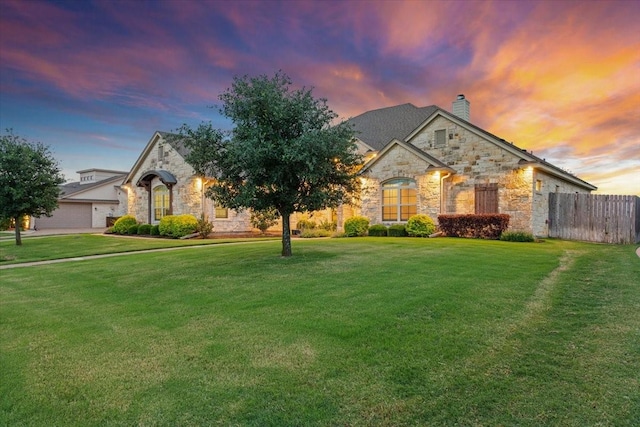 french country inspired facade featuring a front yard, fence, a chimney, and stone siding