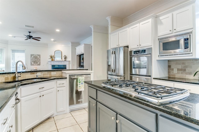 kitchen with appliances with stainless steel finishes, a sink, dark stone counters, decorative backsplash, and ornamental molding