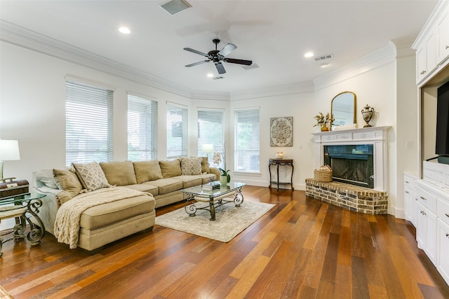 living area featuring dark wood-style flooring, a brick fireplace, a ceiling fan, visible vents, and ornamental molding