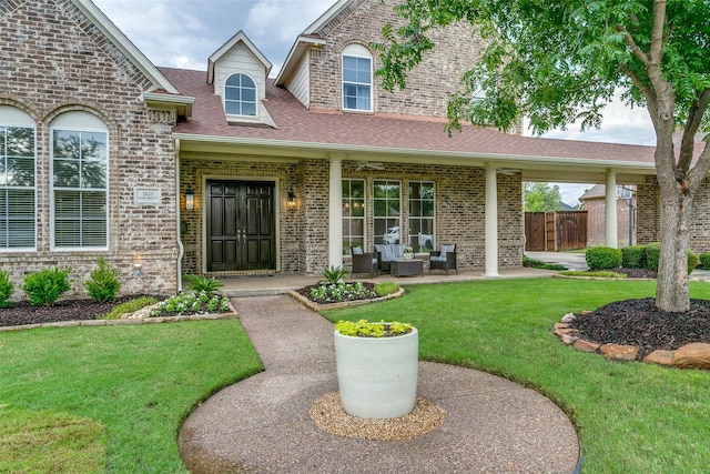 doorway to property with fence, a shingled roof, brick siding, an outdoor hangout area, and a yard