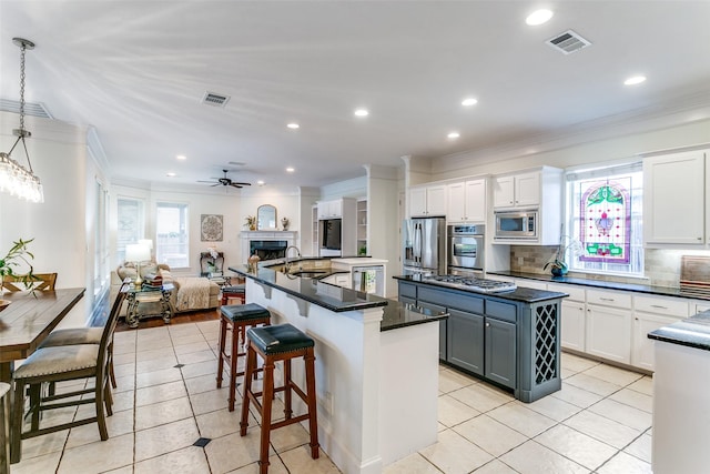 kitchen featuring a kitchen island with sink, stainless steel appliances, open floor plan, visible vents, and ornamental molding