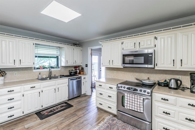 kitchen with crown molding, a sink, light countertops, stainless steel appliances, and tasteful backsplash