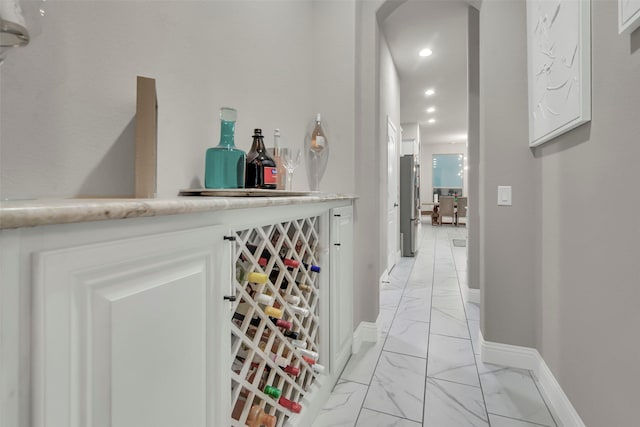 bar featuring a dry bar, arched walkways, marble finish floor, freestanding refrigerator, and baseboards