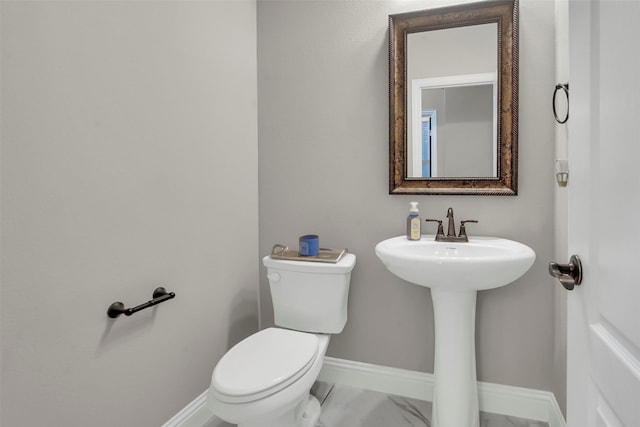 half bathroom with baseboards, marble finish floor, and toilet