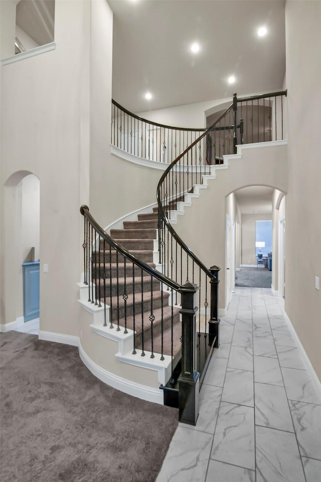stairway with arched walkways, recessed lighting, and a towering ceiling