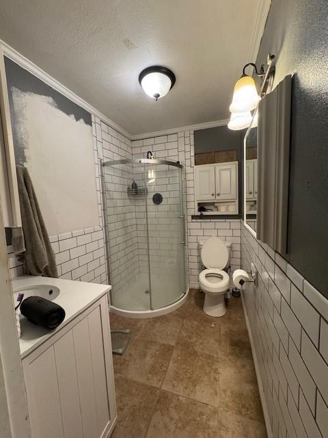 405 E Lee St, Rotan, TX 79546 - bathroom with toilet, a wainscoted wall, tile walls, a shower stall, and ornamental molding