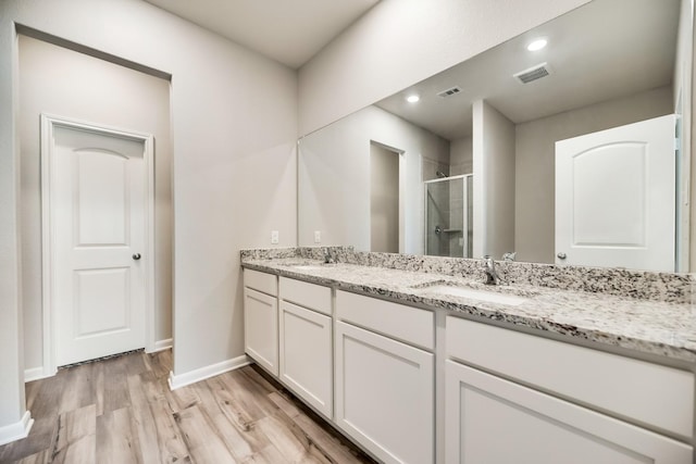 bathroom featuring visible vents, double vanity, wood finished floors, a sink, and a stall shower