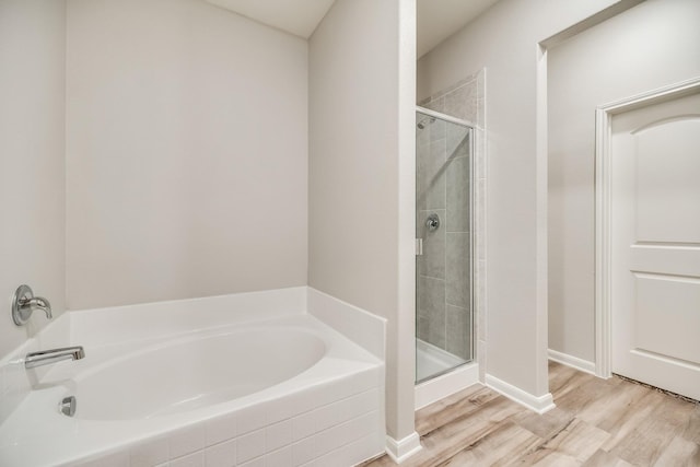 full bath featuring wood finished floors, baseboards, a bath, and a shower stall
