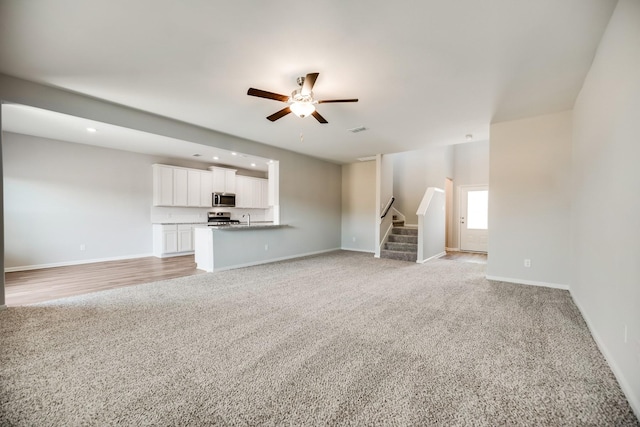 unfurnished living room with a ceiling fan, light colored carpet, stairway, baseboards, and recessed lighting